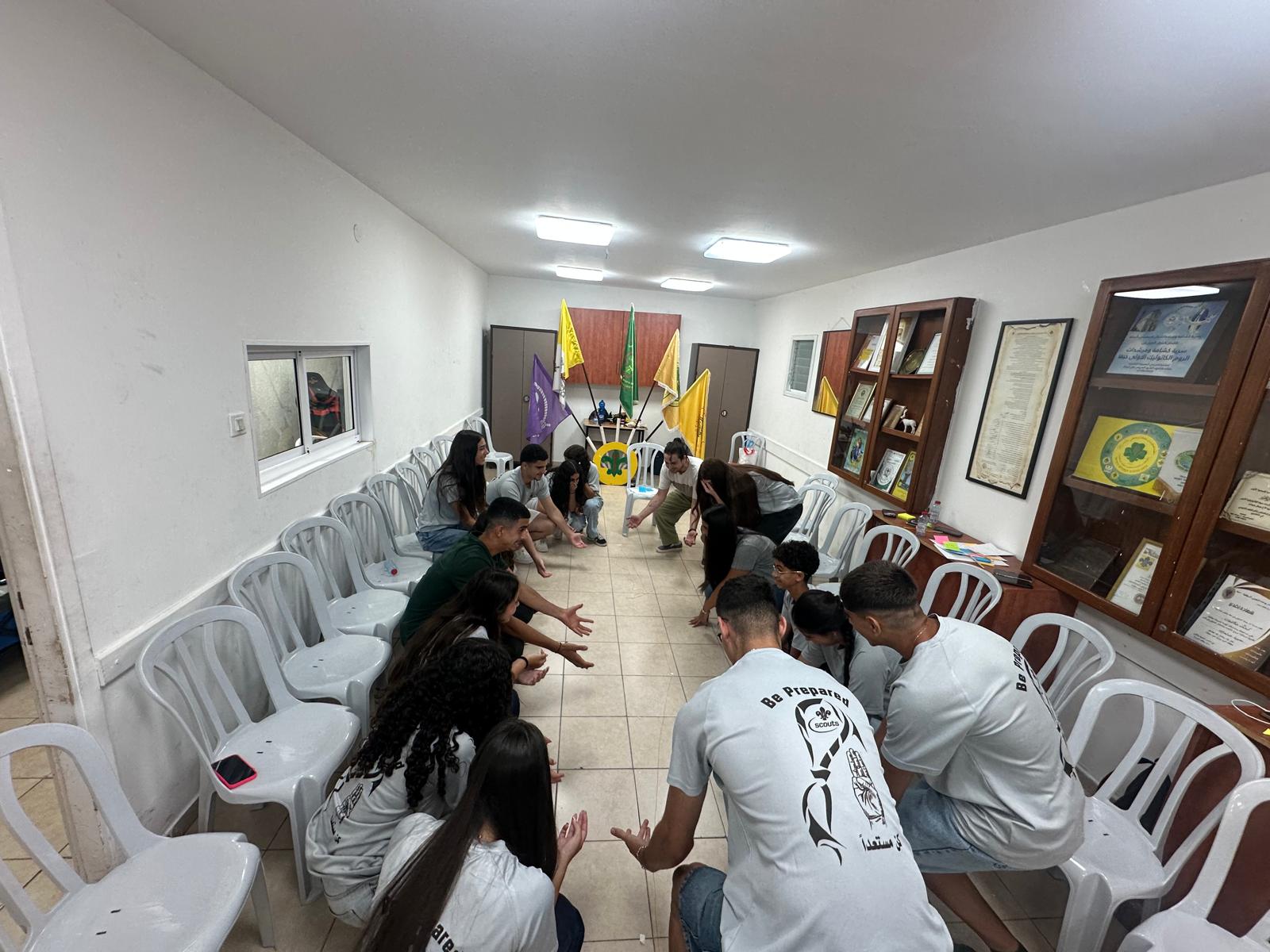 Participants crouch in a circle during a group game, wearing scout shirts reading 'Be Prepared'.