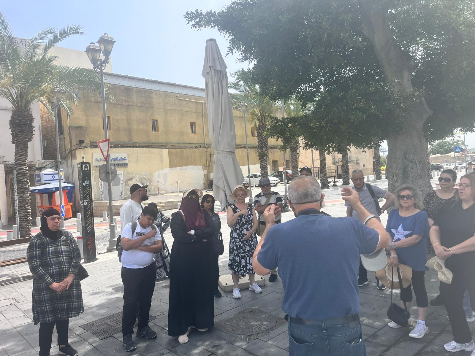 A guided walk in old Haifa, a group listening to a guide beside historic buildings.